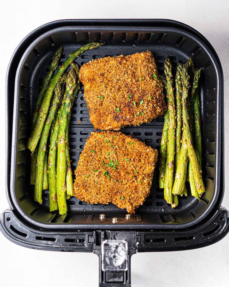 two pieces of meat and asparagus in a air fryer with seasoning