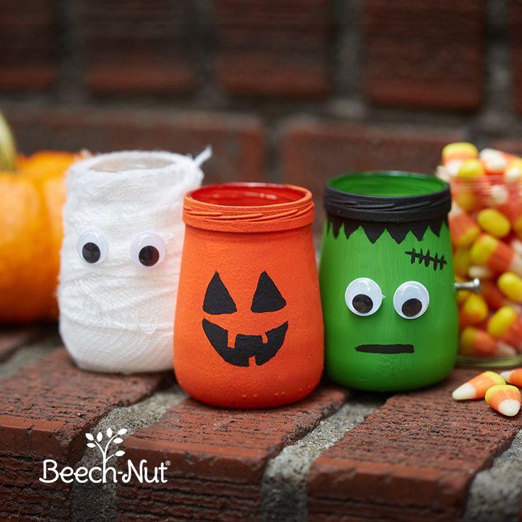 three mason jars decorated with halloween faces and candy corn on the side of a brick wall