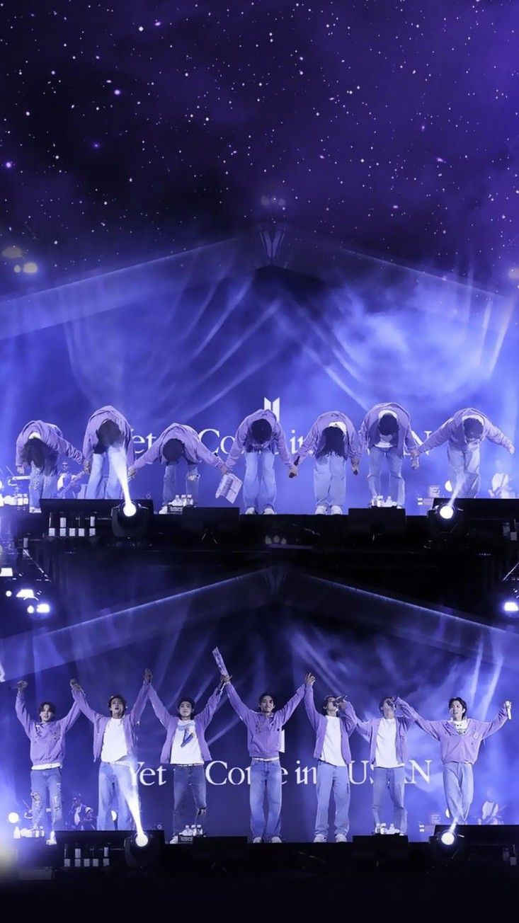 group of people standing on stage with their arms in the air and lights behind them