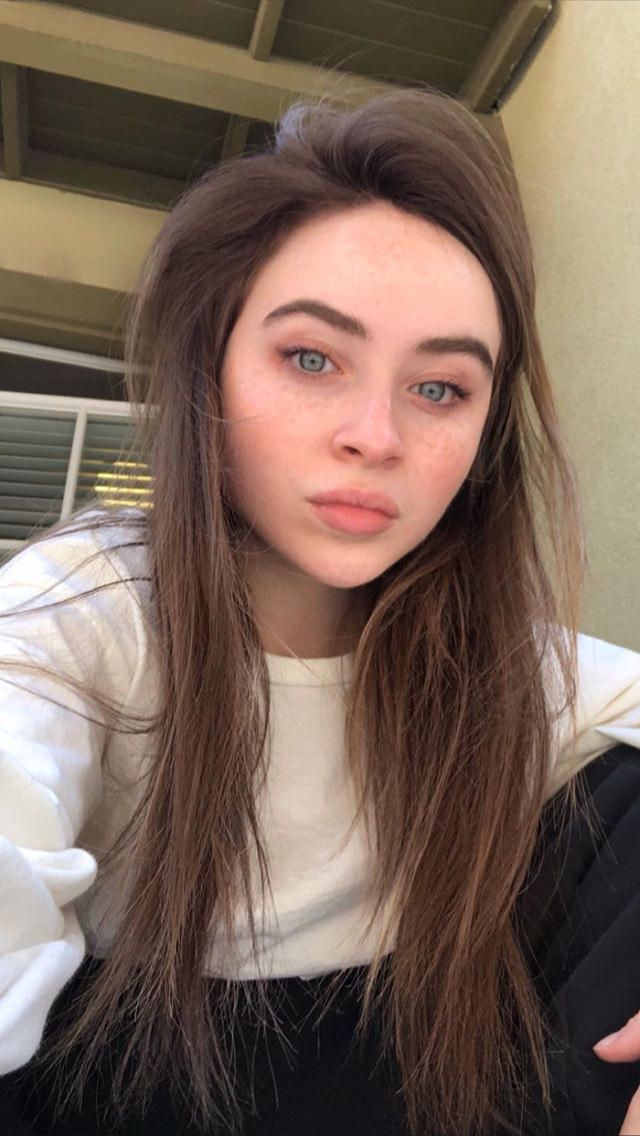 a woman with long hair and blue eyes posing for a selfie in front of a building