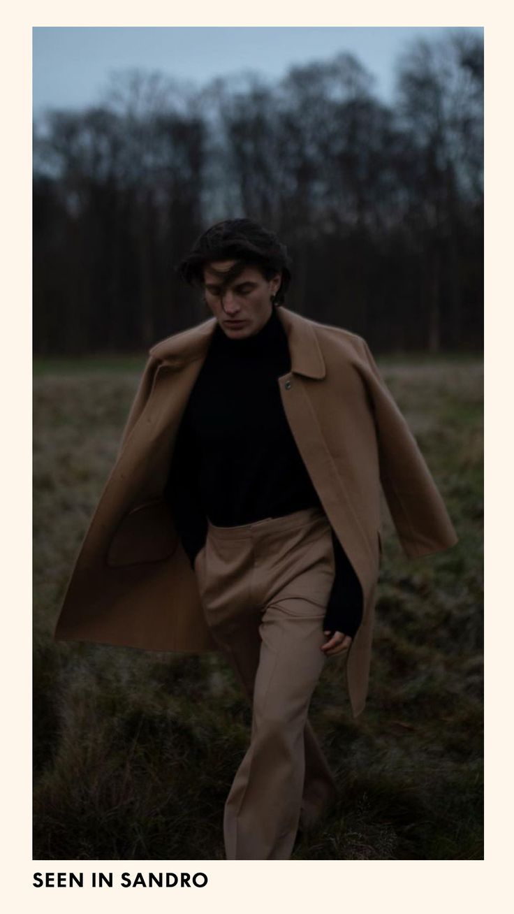 a man walking across a field wearing a brown coat and black turtle - neck sweater