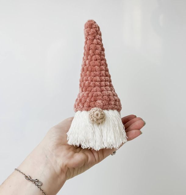 a hand holding a crocheted gnome hat with white and pink yarn on it