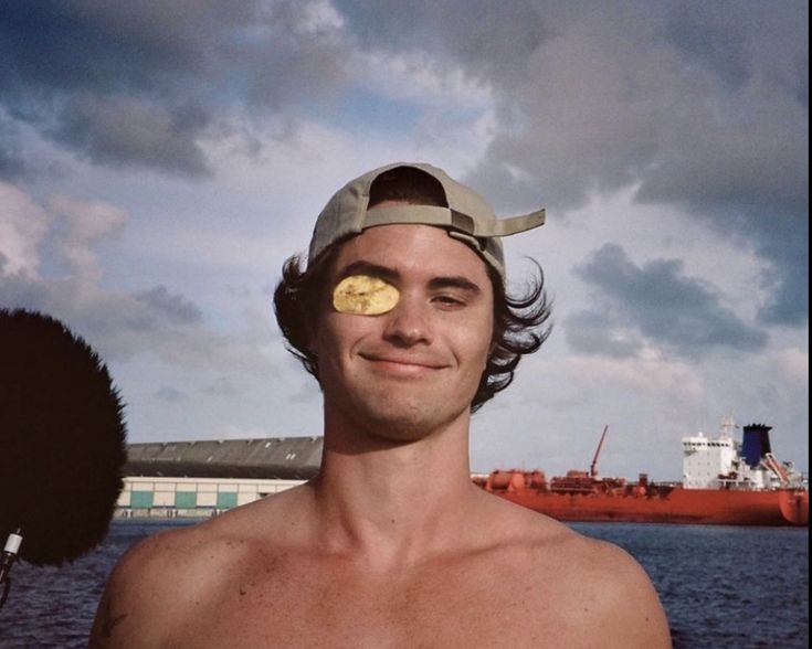 a man wearing a hat with a banana on it's face in front of a large cargo ship