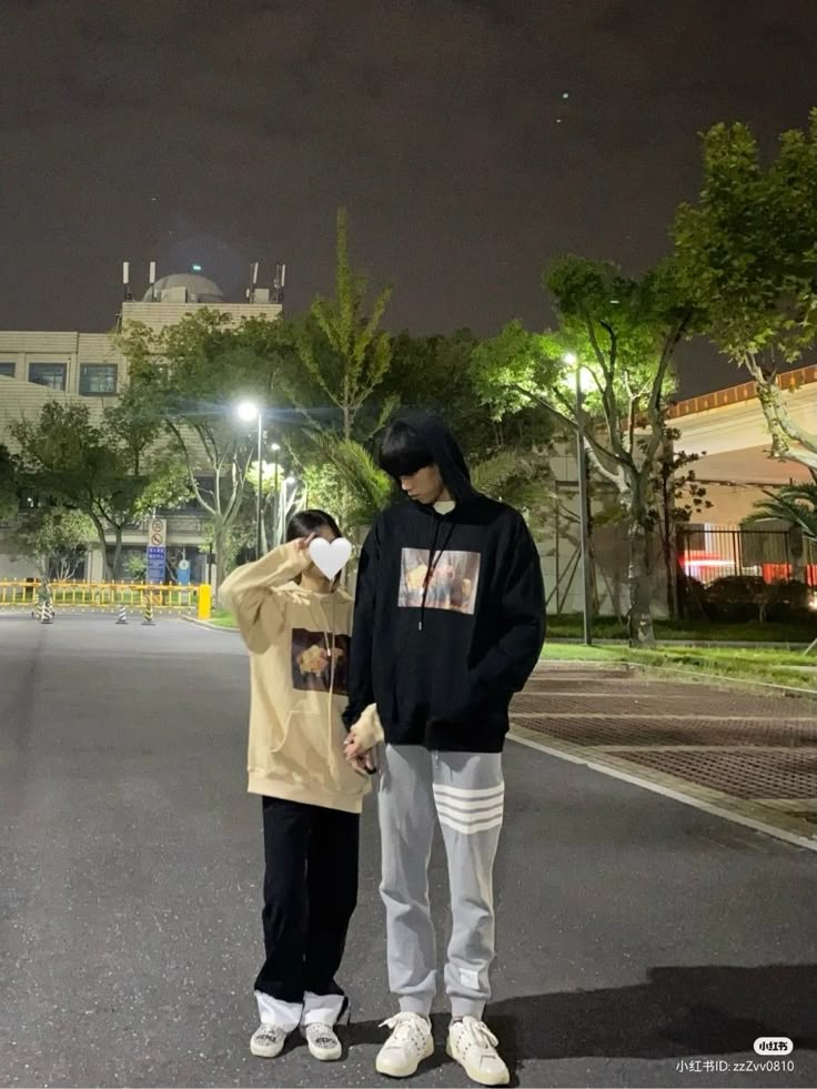 two people standing in the middle of an empty street at night, one wearing a hoodie