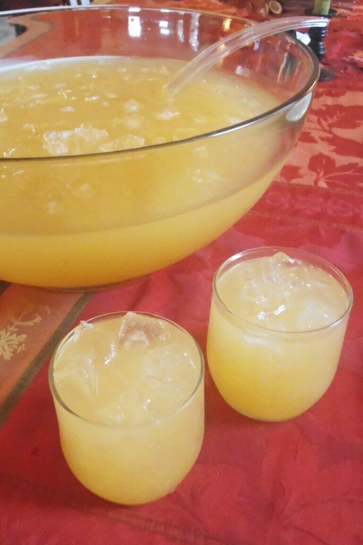 two glasses filled with liquid sit on a table next to a bowl full of orange juice