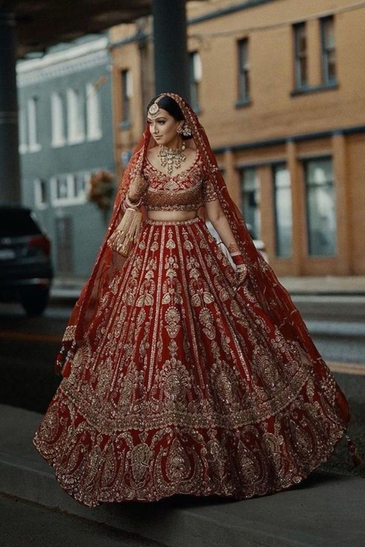 a woman in a red and gold bridal gown is walking down the street with her hand on her hip