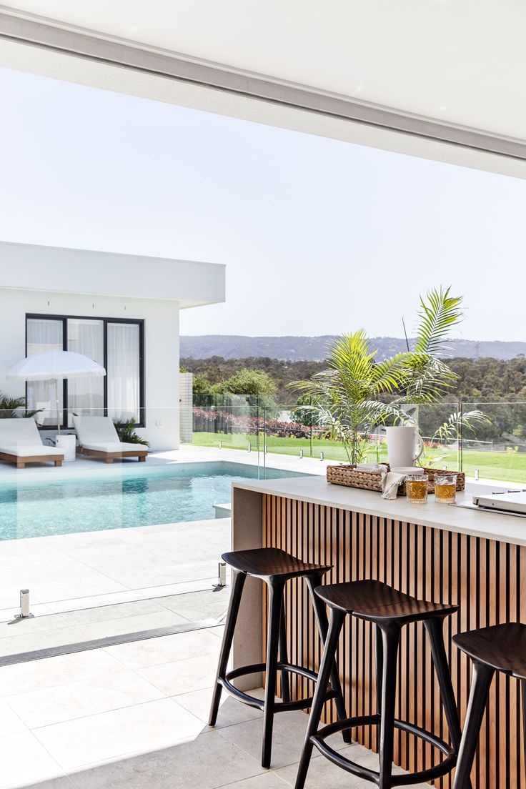 an outdoor bar with stools next to a swimming pool and large open space for entertaining