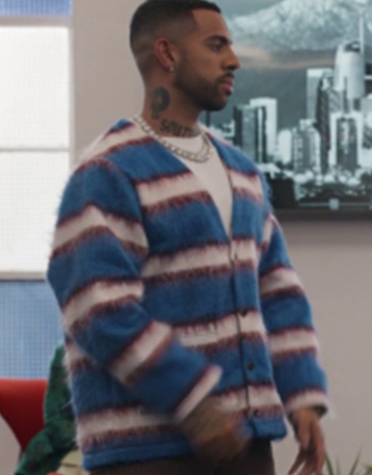 a man in a blue and white striped cardigan standing next to a desk with a laptop on it