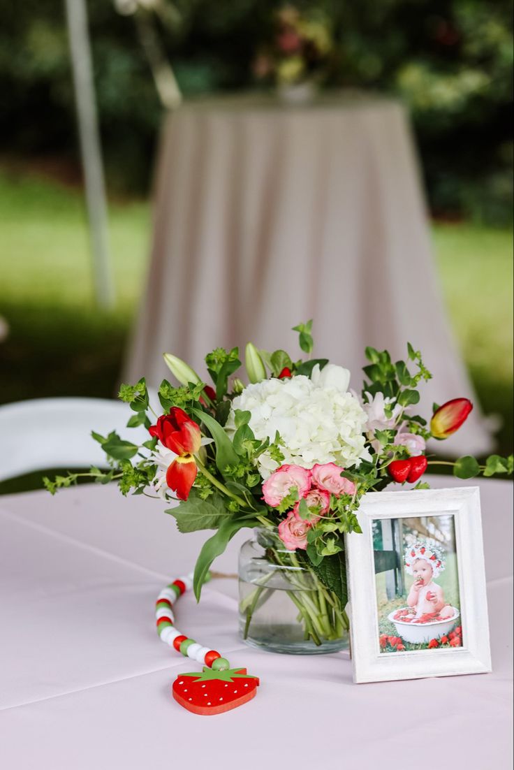 a vase filled with flowers sitting on top of a table next to a framed photo