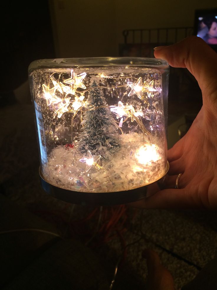 someone is holding up a jar with lights in it and some snow on the ground