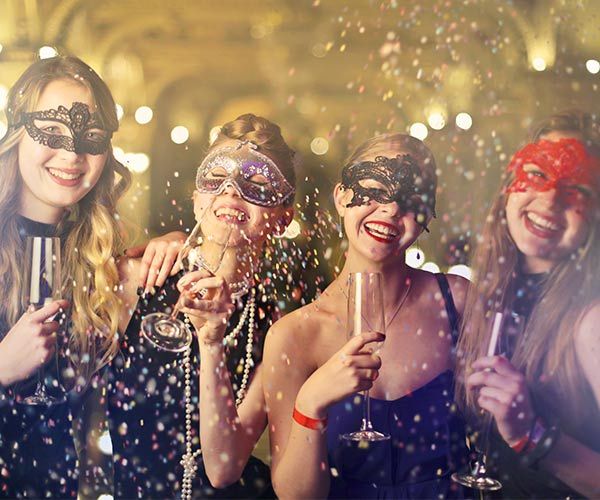 three women wearing masks and holding champagne flutes in front of confetti falling from them