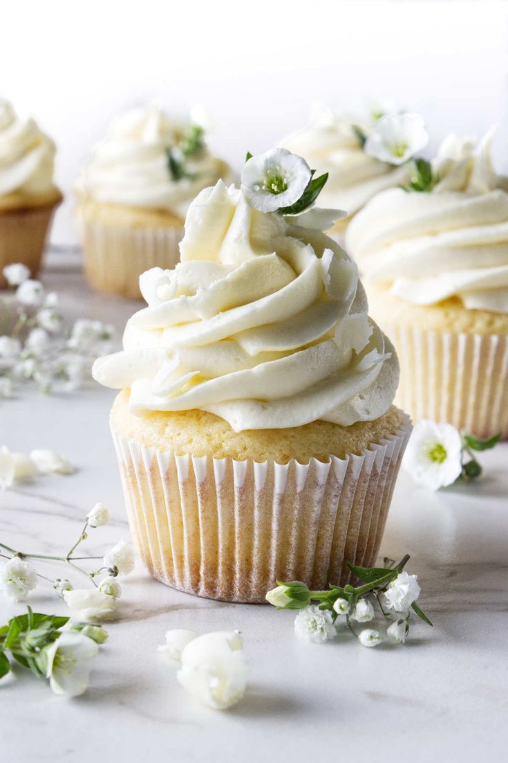 cupcakes with white frosting and flowers on the table