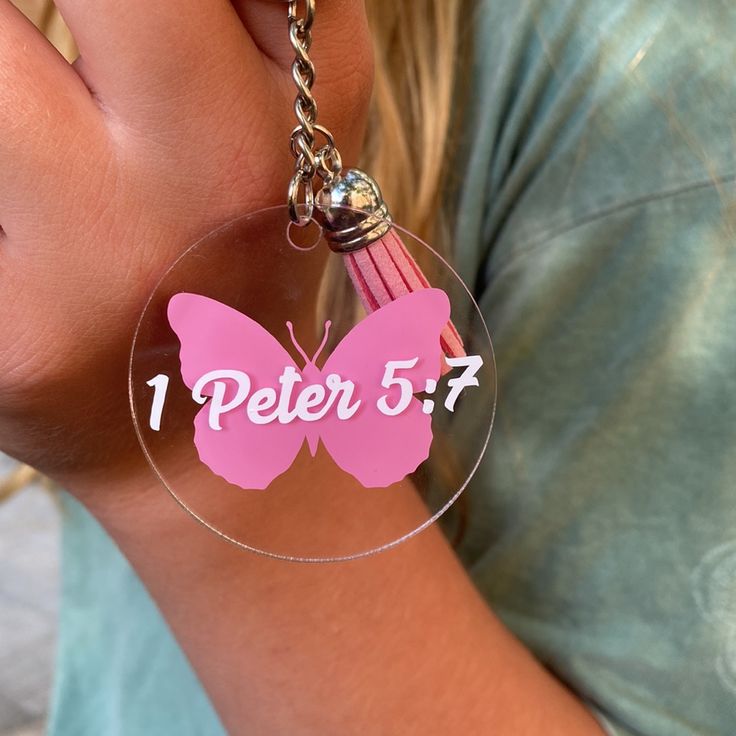 a girl holding a pink butterfly keychain with the word peter 5 7 on it