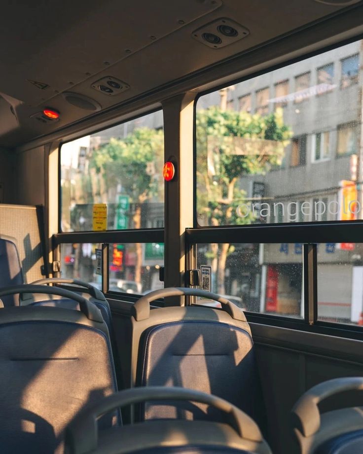 the inside of a bus with empty seats in front of windows and buildings behind it