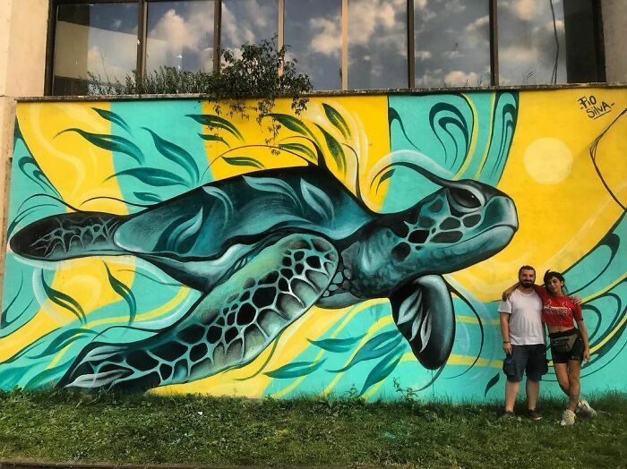 two people standing in front of a wall painted with a mural of a sea turtle