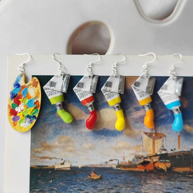 five colorful earrings hanging from hooks in front of an image of a boat and ship