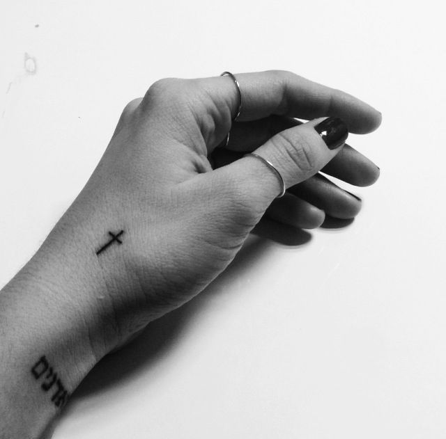 a person's hand with a cross tattoo on the middle of their left arm