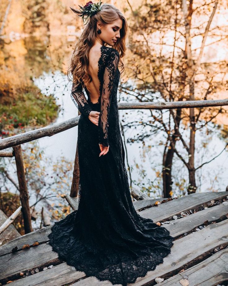 a woman in a black dress standing on a wooden bridge with her back to the camera