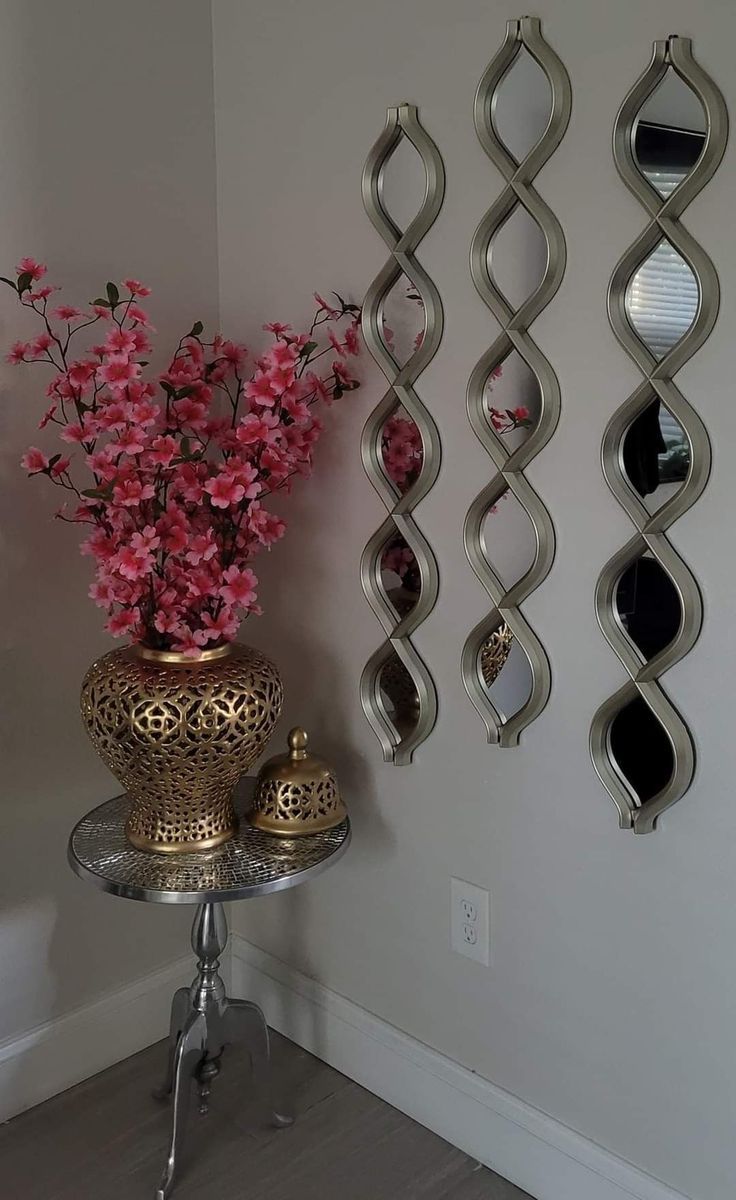 a vase filled with pink flowers sitting next to two metal wall hangings on a wall