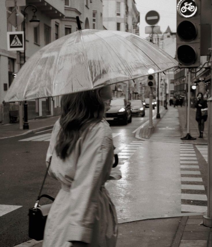 a woman walking down the street with an umbrella over her head while it is raining