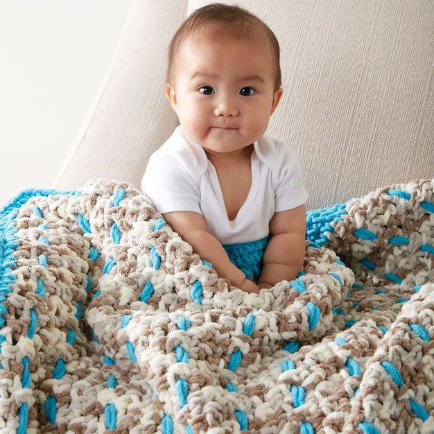 a baby sitting on top of a couch under a blue and white blanket, smiling at the camera