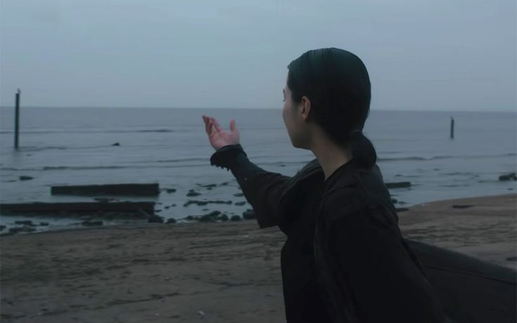 a man standing on top of a beach next to the ocean holding his hands up