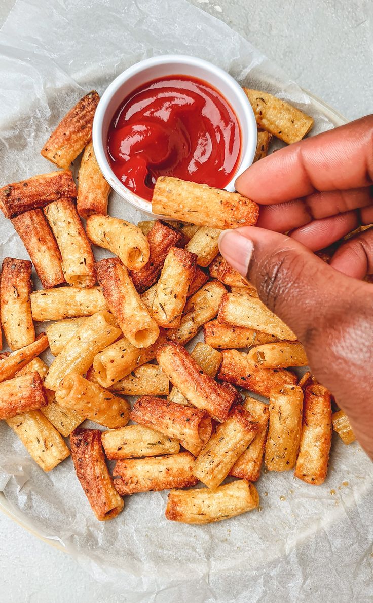 someone is dipping ketchup into some fries on a white plate with parchment paper