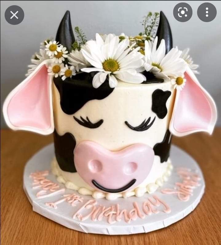 a cow cake with daisies in its mouth on top of a wooden table next to a wall