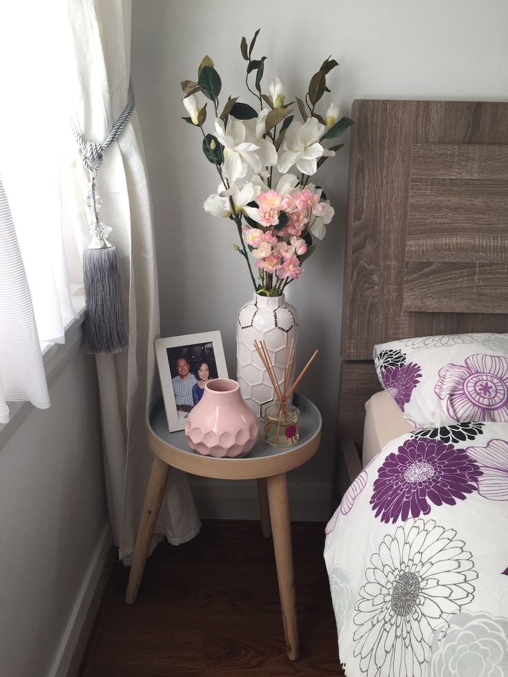 a vase with flowers sitting on a small table next to a bed in a bedroom