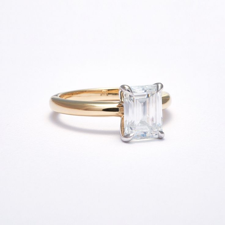 a gold ring with an emerald cut diamond in the center, on a white background