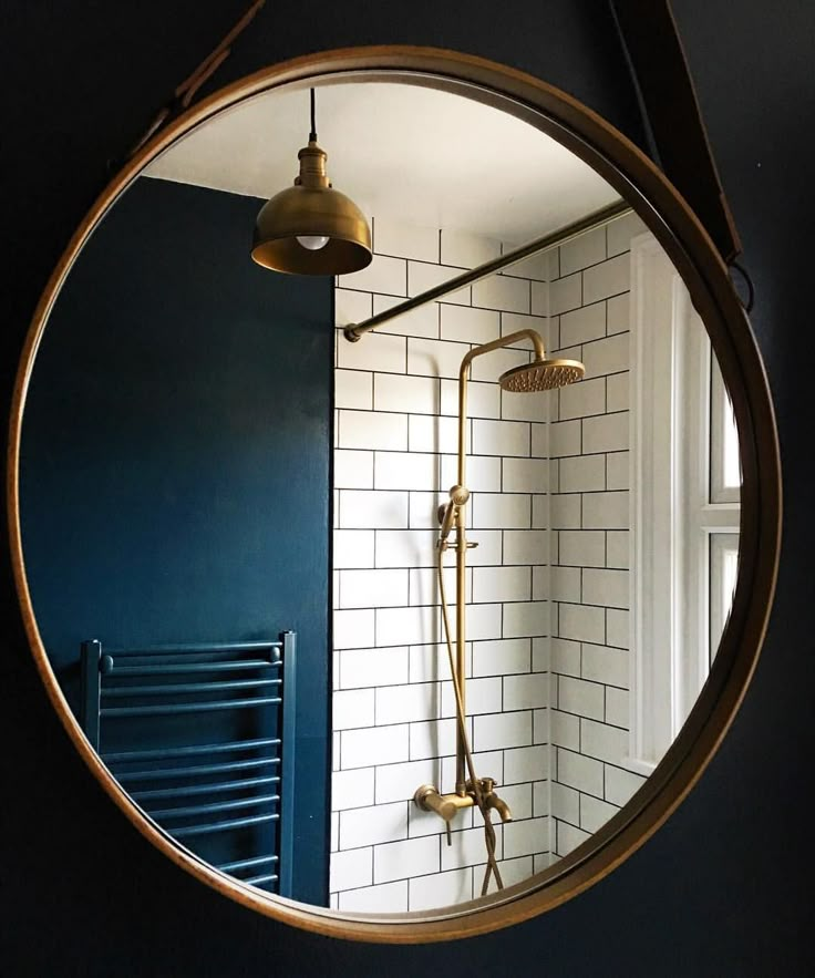 a round mirror hanging on the side of a wall next to a bathtub and radiator