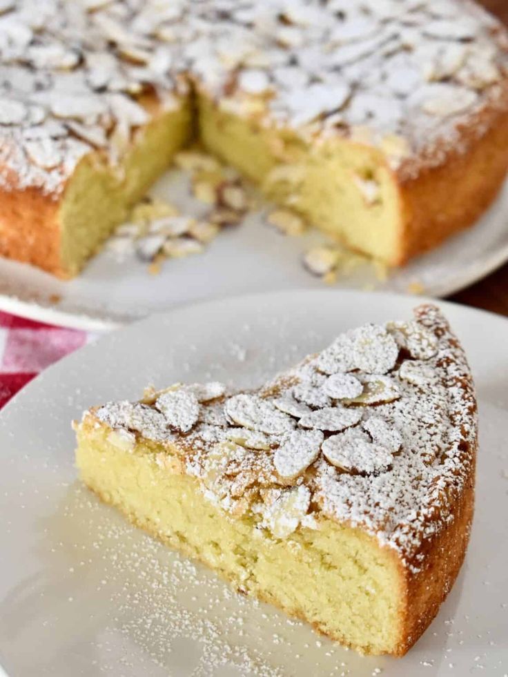 a piece of cake on a white plate with powdered sugar over it and another slice in the background