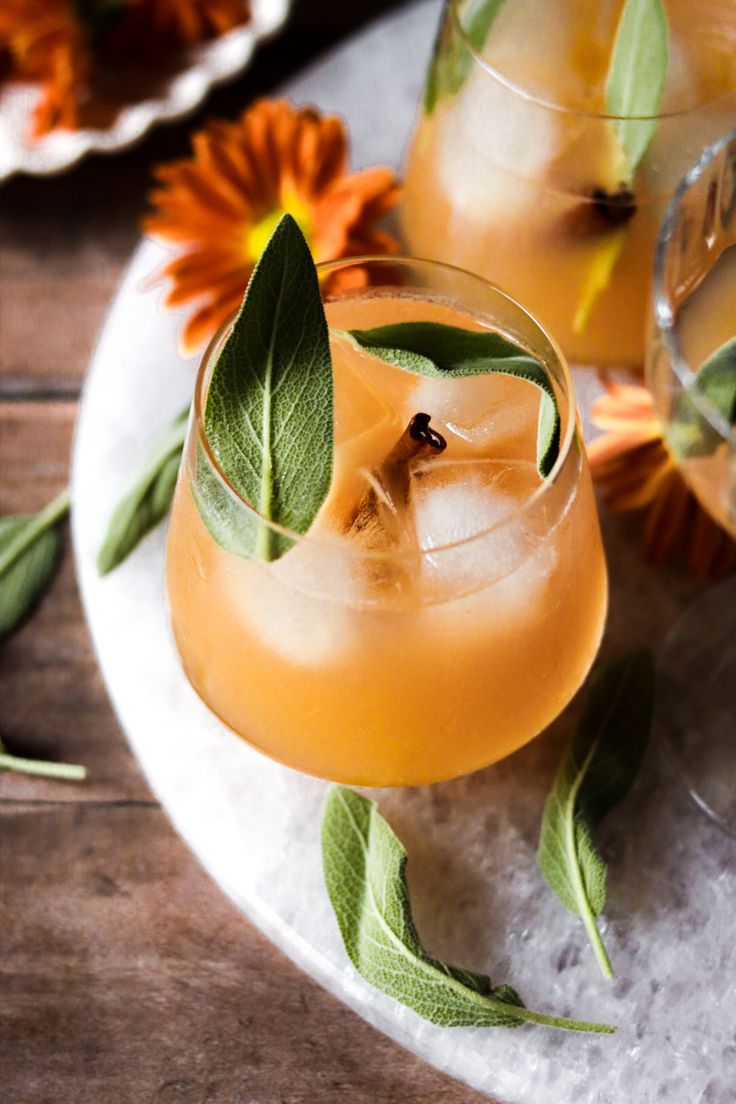 two glasses filled with drinks sitting on top of a white plate next to orange flowers