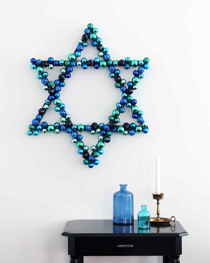 a star of david made out of beads on a wall above a table with a blue vase and candle