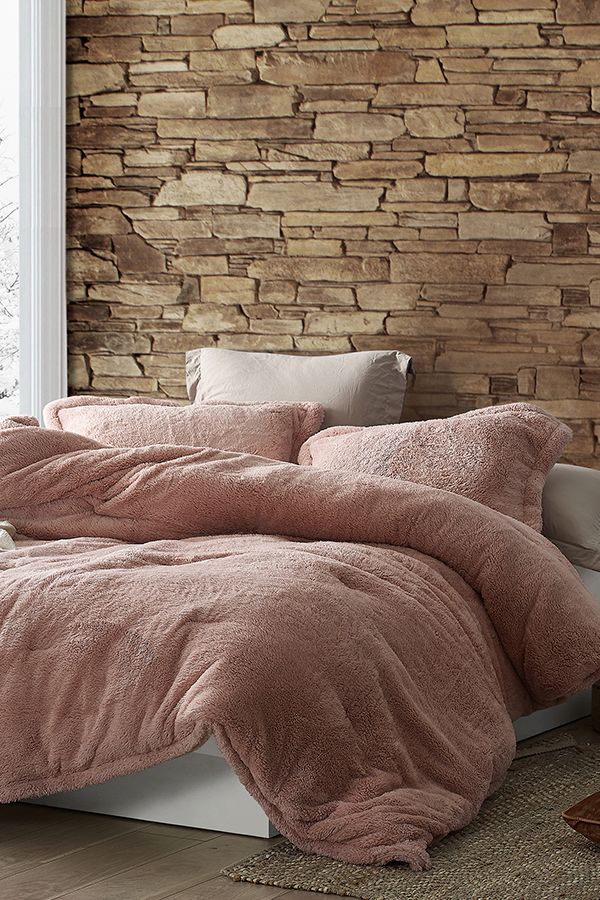 a bed with a pink comforter and pillows in front of a bricked wall