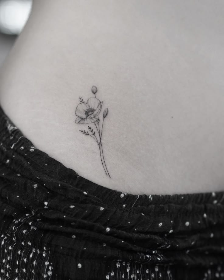 a woman's stomach with a single flower tattoo on her lower back side ribcage