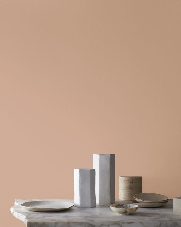 a table with plates and vases on it in front of a peach colored wall