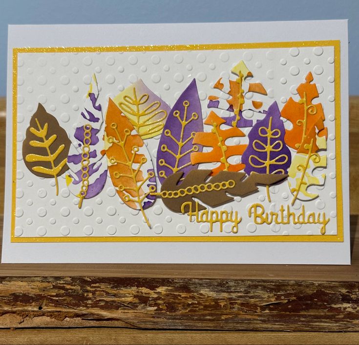 a happy birthday card with leaves on the front and bottom, sitting on top of a piece of wood