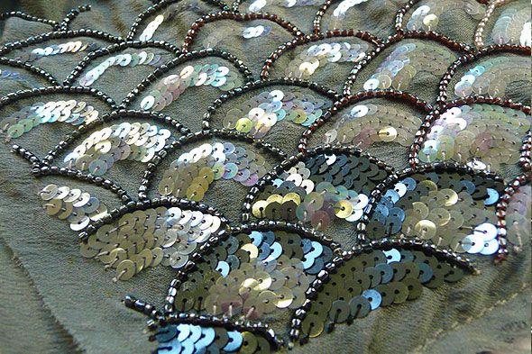 sequins and beads are on the back of a black fabric with silver scales