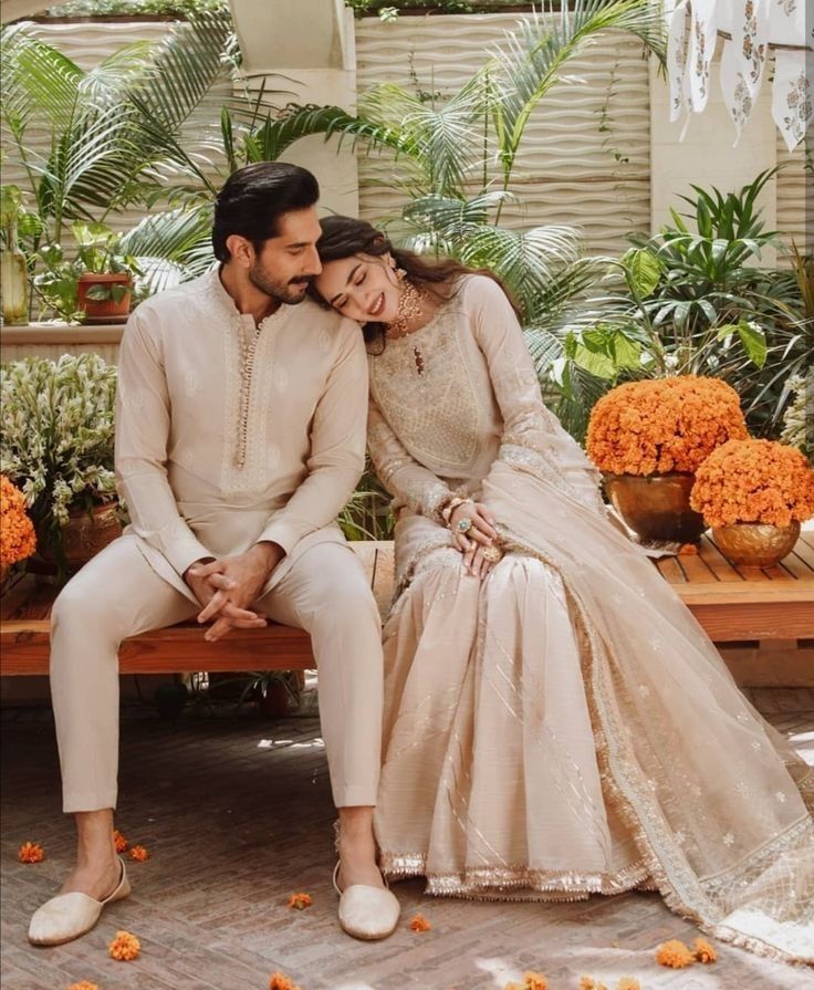 a man and woman sitting on a bench next to each other in front of flowers