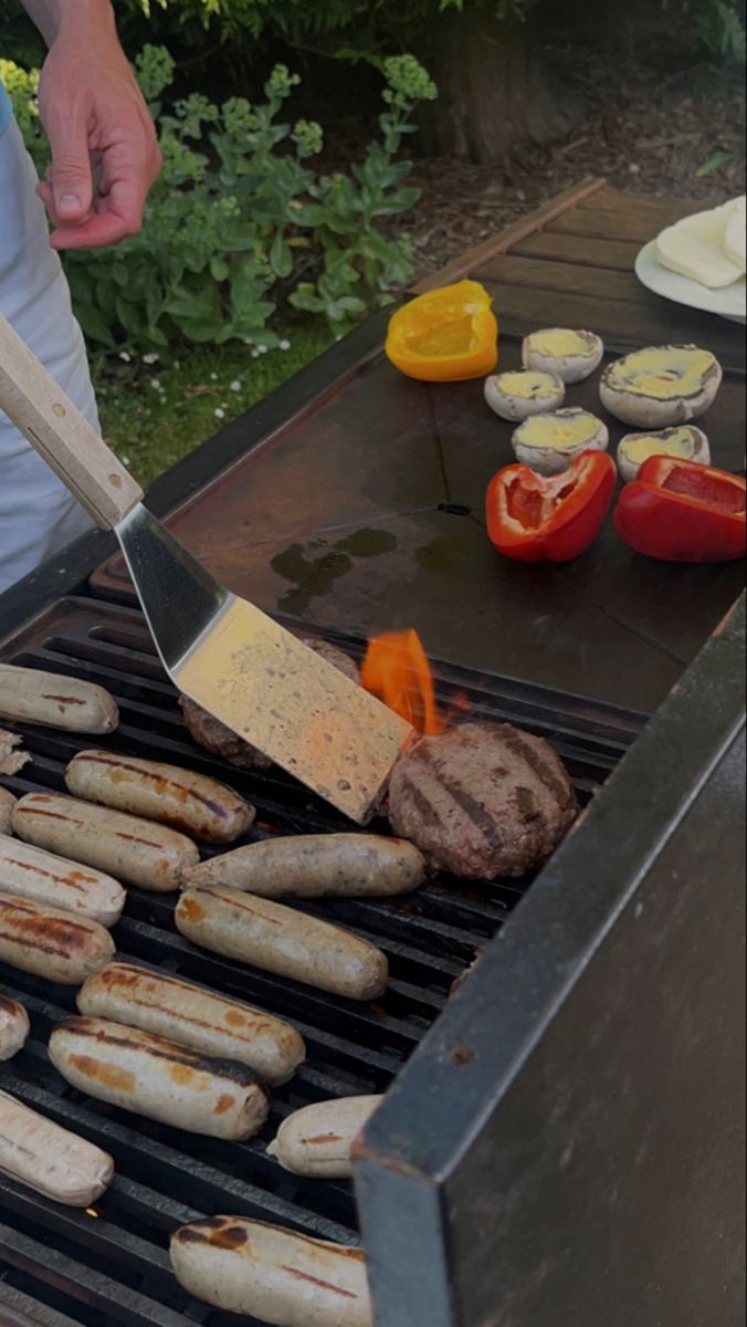 a man grilling hot dogs and hamburgers on an outdoor grill with tongs