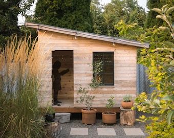 a small wooden shed with potted plants outside