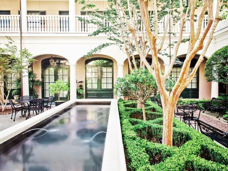 an outdoor courtyard with tables, chairs and a water feature in the center surrounded by greenery