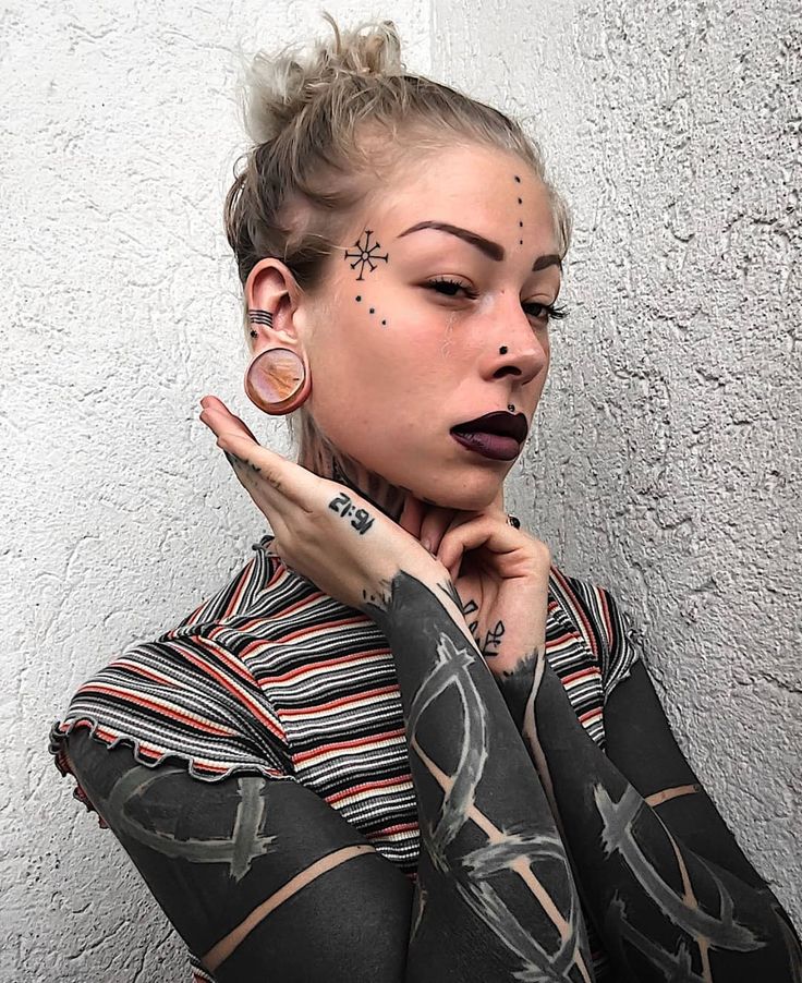 a woman with tattoos and piercings on her face is posing for the camera in front of a white wall