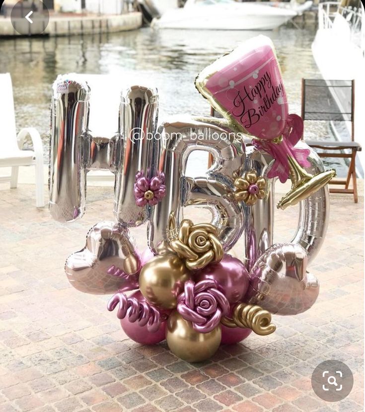 a balloon shaped like the letter b with flowers and balloons attached to it in front of a body of water