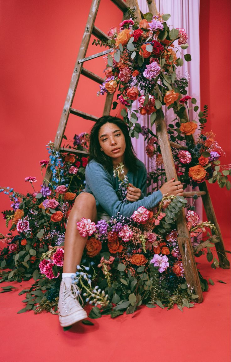 a woman sitting on top of a ladder surrounded by flowers