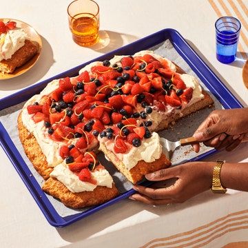 a person cutting into a cake with strawberries and blueberries on it