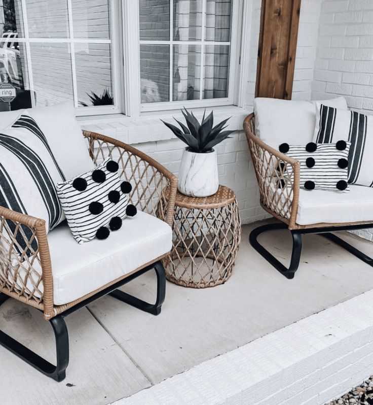 two wicker chairs with black and white pillows sit on the front porch next to a potted plant