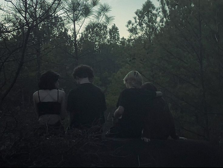 three people sitting on a rock in the woods looking at trees and sky, with one person holding onto another's back