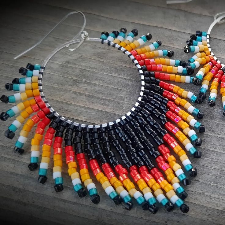 a pair of multicolored beaded earrings sitting on top of a wooden table